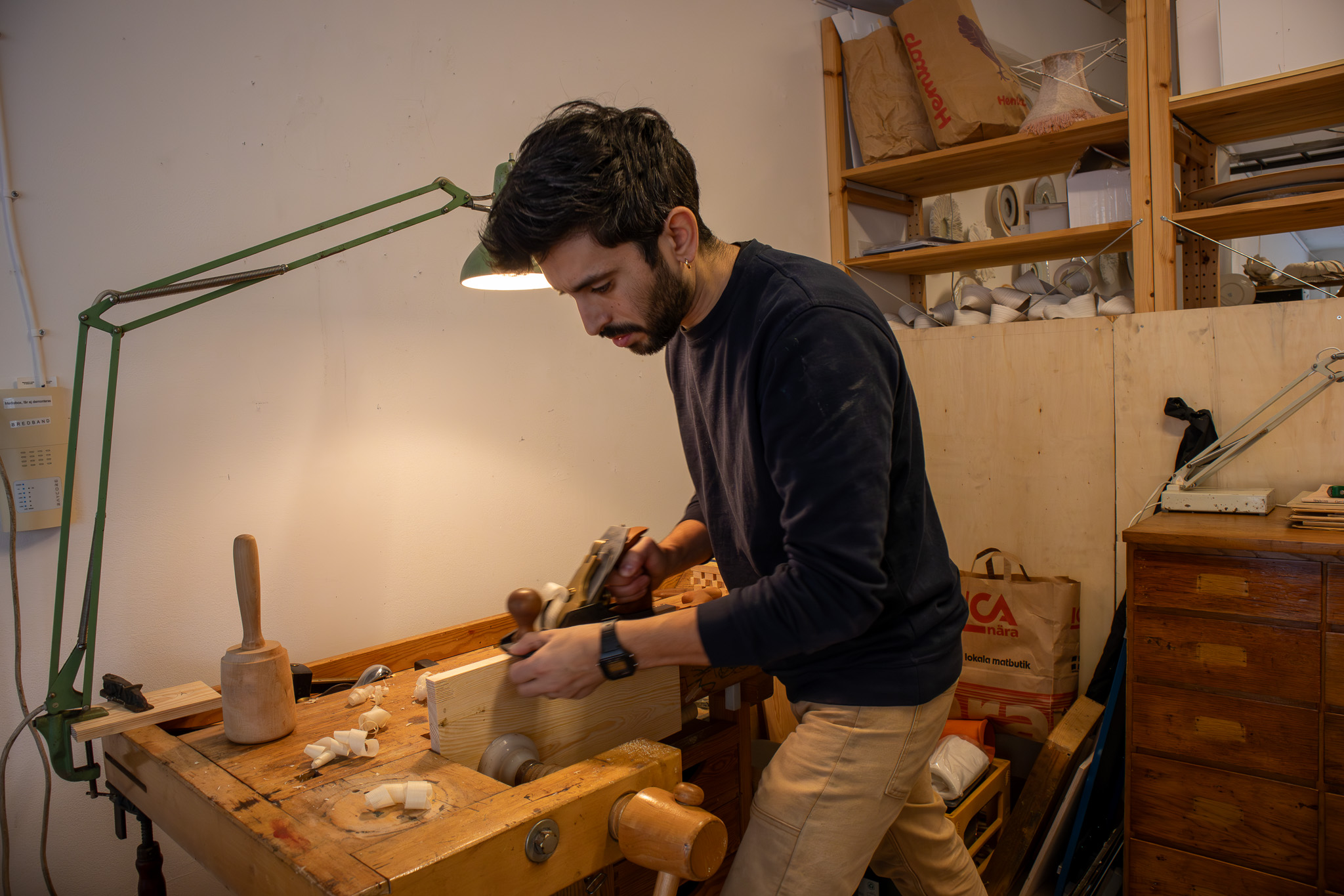 En man i blå tröja hyvlar en träbit